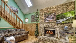Ein gemütliches Wohnzimmer mit Kamin aus Stein, einer Holztreppe und einer grünen Wand.
