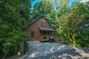 A wooden cabin with a porch, surrounded by trees.