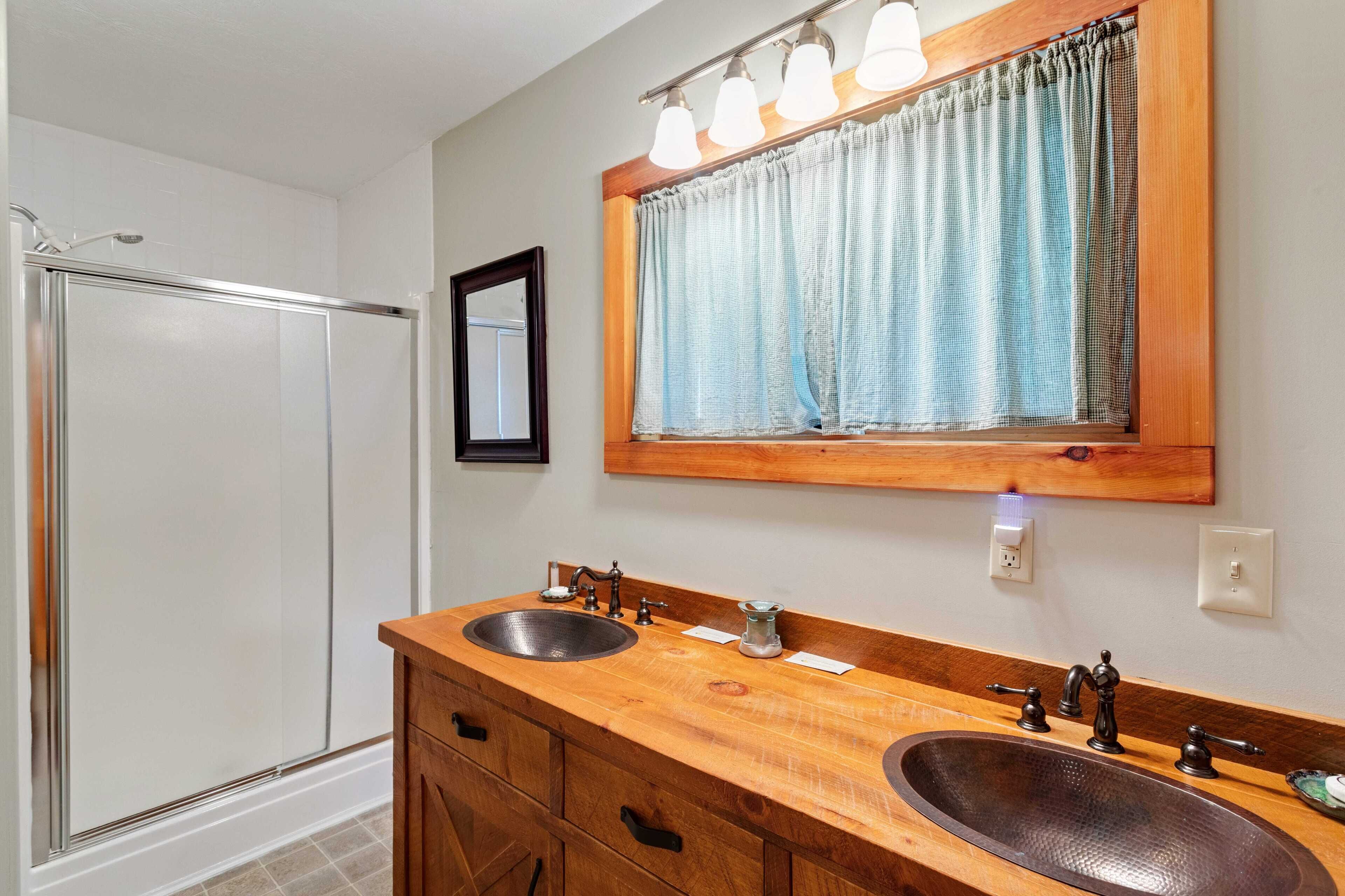 A bathroom with a wooden vanity, two sinks, a mirror, and a shower.