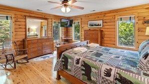 Un dormitorio de cabaña de madera con cama, cómoda, silla y ventilador de techo.