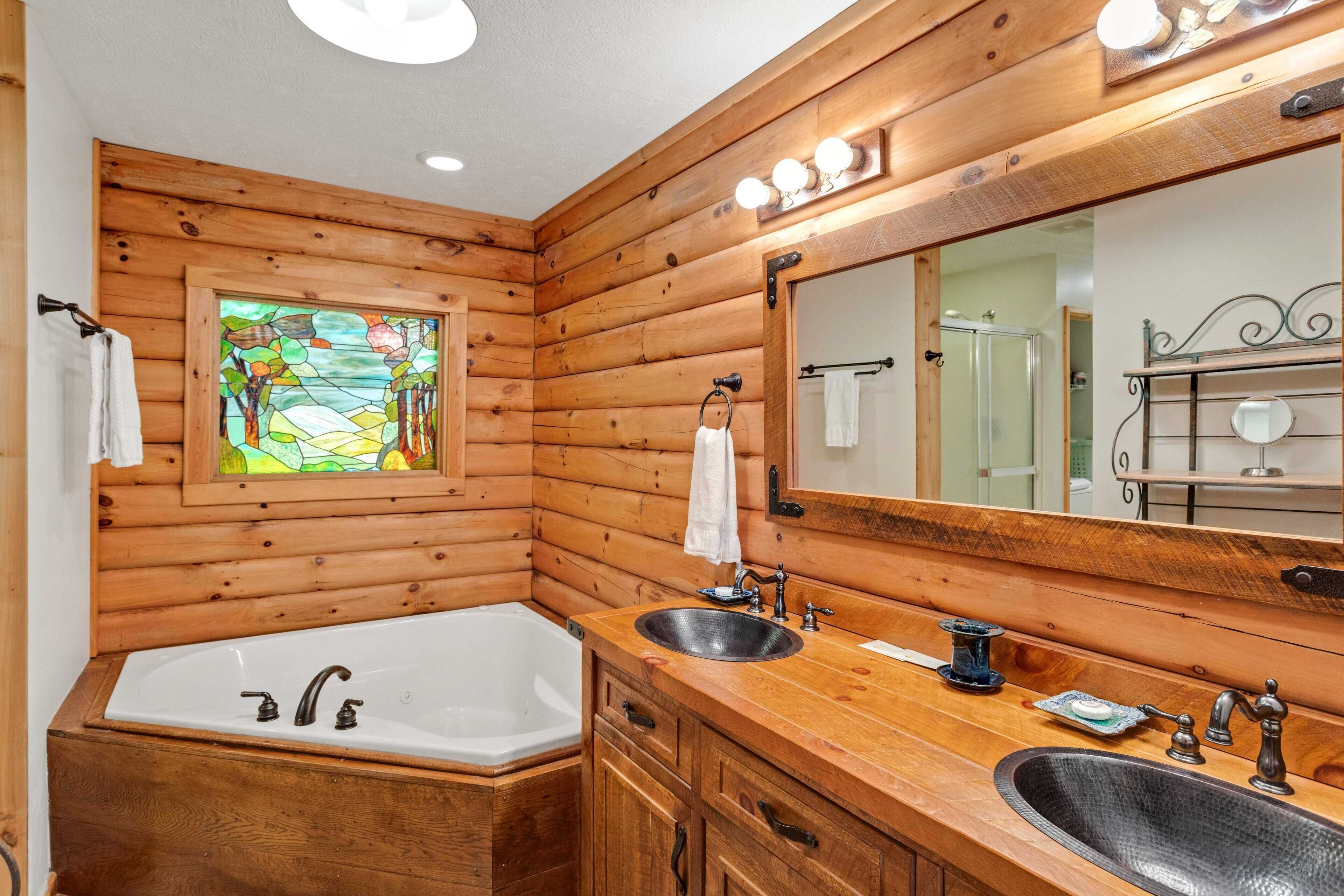 A wooden cabin bathroom with a large bathtub, two sinks, and a mirror.