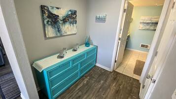 A hallway with a teal vanity, a painting on the wall, and a door leading to another room.