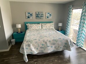 A bedroom with a bed, two bedside tables, a wall with artwork, and a window with curtains.