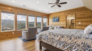Un dormitorio con una cama grande, ventilador de techo y vistas a las montañas a través de amplias ventanas.