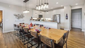Una cocina moderna con armarios blancos, una mesa de comedor de madera y luces colgantes.