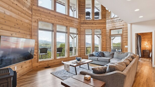 Amplia sala de estar con una gran televisión de pantalla plana, pisos de madera y una zona de estar acogedora con un sofá y sillones.