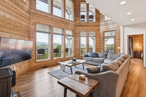 Amplia sala de estar con una gran televisión de pantalla plana, pisos de madera y una zona de estar acogedora con un sofá y sillones.