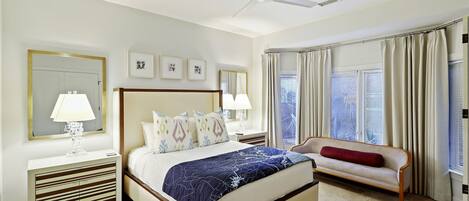 A hotel room with a large bed, a bedside table with a lamp, a chair, and a ceiling fan.
