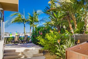 A patio with outdoor seating, a wooden deck, and lush tropical plants. - Villa on the Bay | 1BR Bayfront in Mission Beach (San Diego)