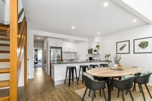 Una cocina moderna con armarios blancos, una isla central con taburetes y una mesa de comedor con sillas.