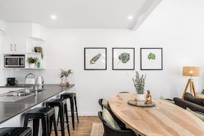 Une cuisine moderne dotée d’un îlot central, de tabourets de bar et d’un coin repas avec une table et des chaises en bois.