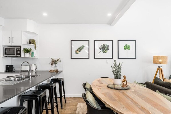 Una cocina moderna con una isla central, taburetes de bar y un comedor con una mesa y sillas de madera.