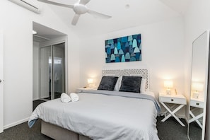 Une chambre d’hôtel comprenant un lit, deux tables de chevet, un ventilateur de plafond, une œuvre d’art accrochée au mur et une porte-fenêtre coulissante donnant accès à la salle de bain.
