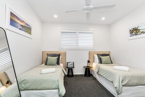 Habitación de hotel con dos camas, un ventilador de techo, una ventana con persianas e imágenes enmarcadas en las paredes.