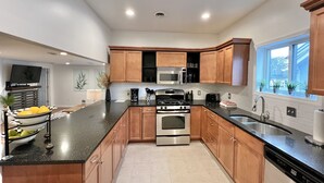 A modern kitchen with wooden cabinets, stainless steel appliances, a black countertop, and a window with plants. -  Fully Furnished Apartment 2 Bedroom-Special rates for 30-night stays or more (Rochester)