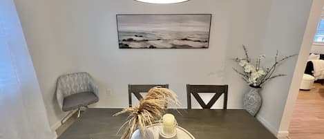 A dining area with a dark wooden table, two chairs, a vase with branches, a candle, and a tray with a rock.