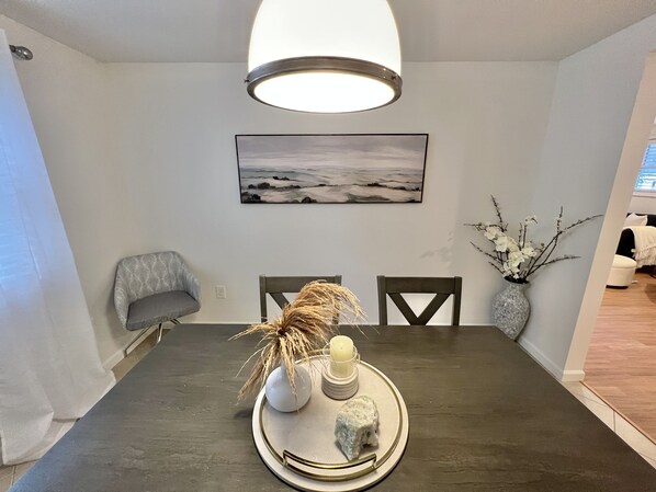 A dining area with a dark wooden table, two chairs, a vase with branches, a candle, and a tray with a rock.