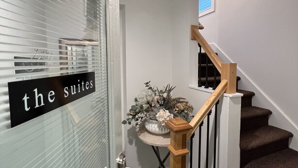 A staircase with a wooden handrail and black balusters, leading to a landing with a small table and a vase of flowers. -  Fully Furnished Apartment 2 Bedroom-Special rates for 30-night stays or more (Rochester)