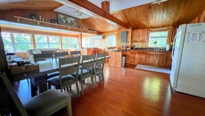 Una cocina amplia con armarios de madera, un comedor con mesa y sillas, y ventanas grandes que dejan entrar luz natural.