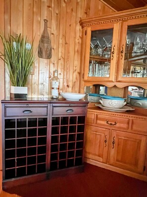 A wooden kitchen with a wine rack, a potted plant, and glassware on shelves.