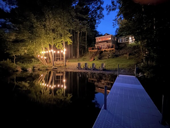 A lakeside property with a dock, a wooden deck, and a house with a large window overlooking the water.