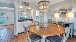 A dining area with a wooden table, chairs, a chandelier, and a kitchen with glass cabinets. - 703 Schooner Court sleeps 7 with Calibogue sound views in Harbour Town. Book your stay today! (Hilton Head Island)