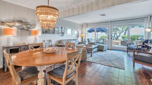 A spacious living area with a wooden dining table, comfortable seating, and a large window offering a view of the outdoors. - 703 Schooner Court sleeps 7 with Calibogue sound views in Harbour Town. Book your stay today! (Hilton Head Island)