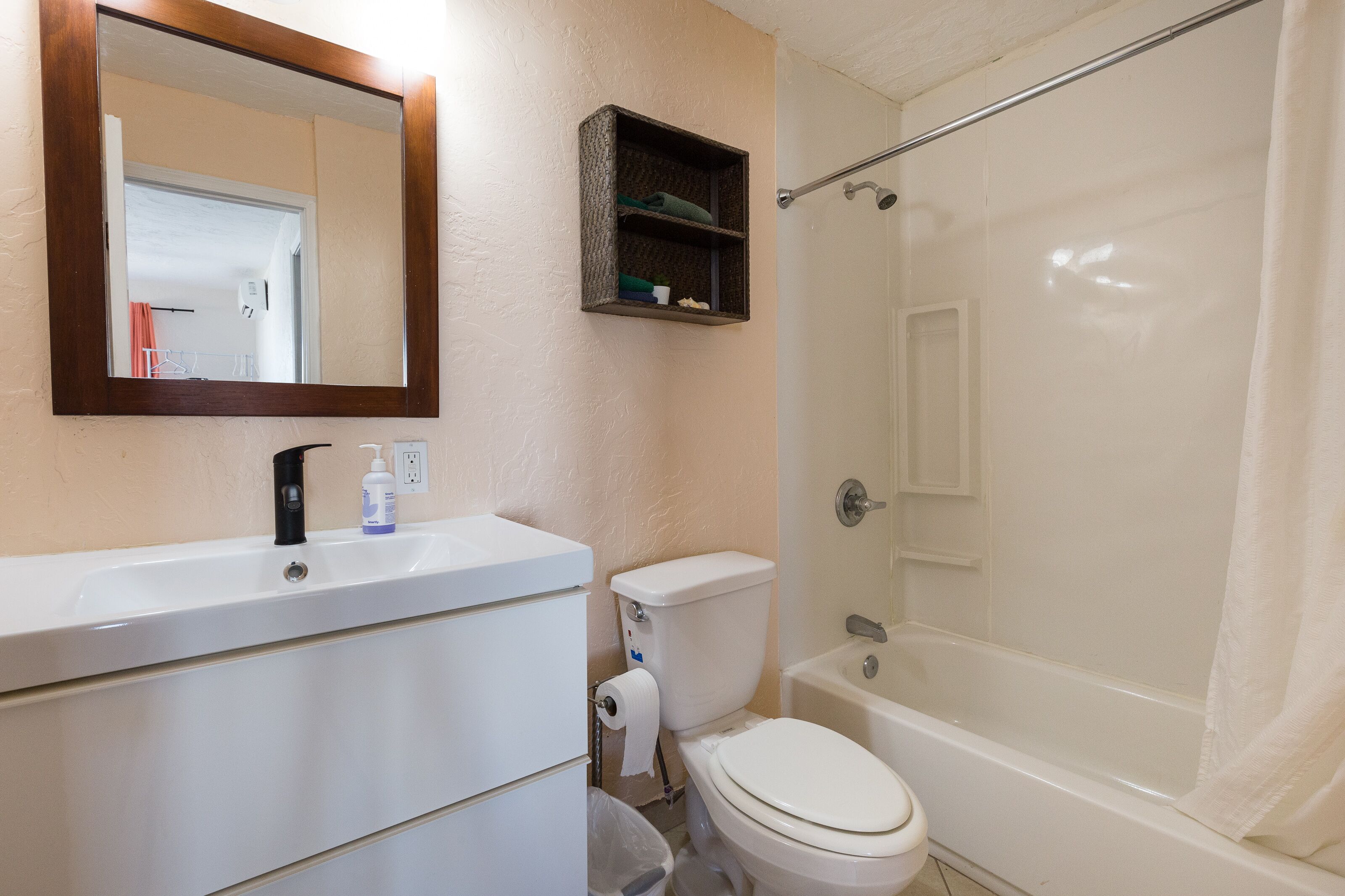 A bathroom with a white sink, toilet, and bathtub. There is a mirror above the sink and a shelf with toiletries.