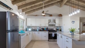 A modern kitchen with white cabinets, stainless steel appliances, and a wooden ceiling.