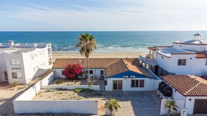 A coastal building with a tiled roof, a palm tree, and a view of the sea.