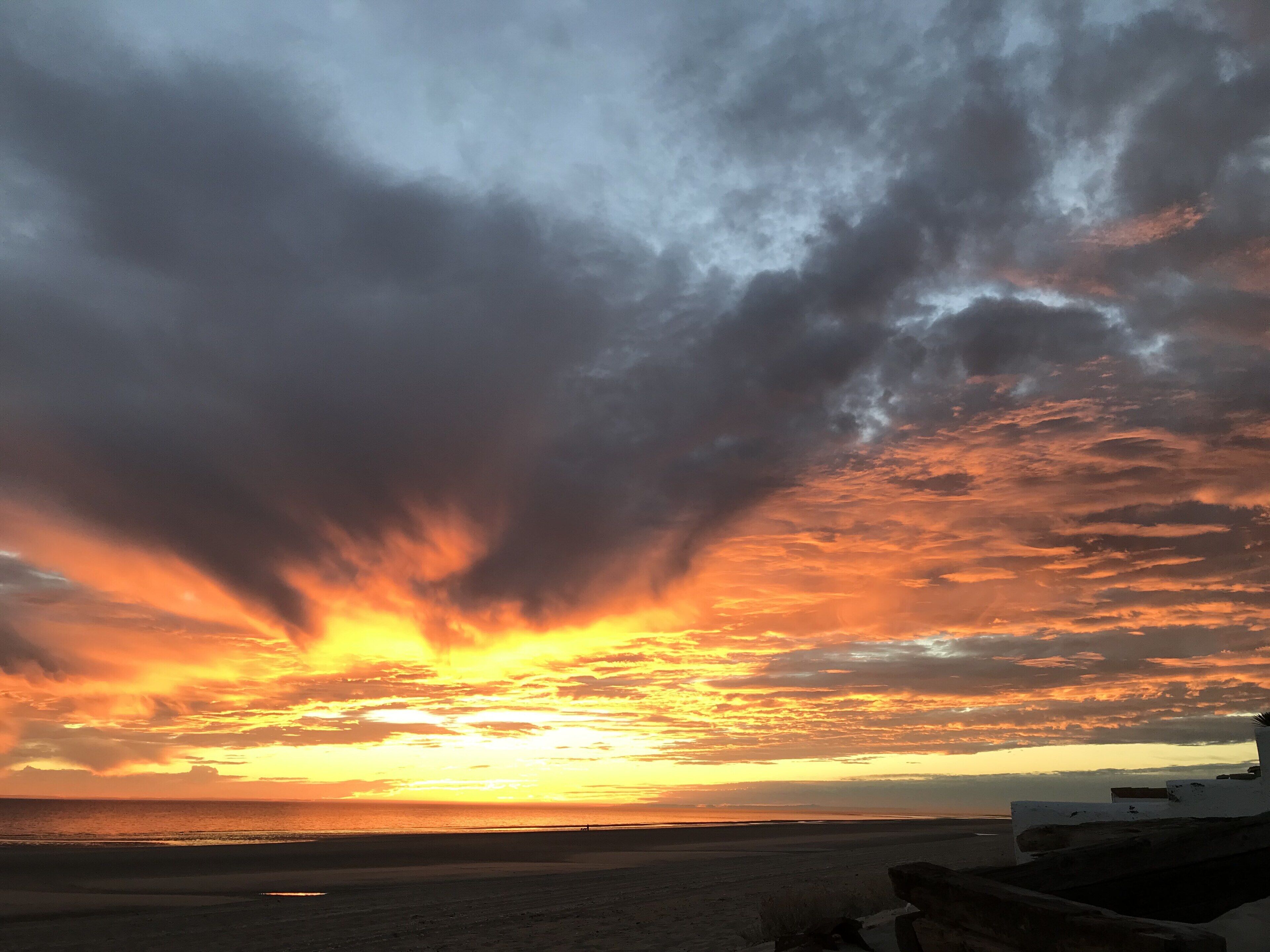 Een strand met een ondergaande zon, wolken en een verre horizon.