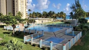 En swimmingpool omgivet af palmer og en høj bygning i baggrunden.