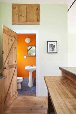 Ein Badezimmer mit Holztür, Waschbecken in Weiß und einem gerahmten Spiegel an der Wand.