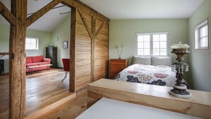 Een ruime kamer met een houten plafond, een bed met bloemenbedrukking, een rode stoel en een houten dressoir.