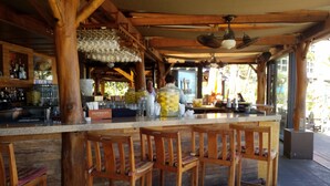 A rustic bar area with wooden chairs, a bar counter, and a ceiling fan. -  Location! Golf, Swim, Surf & WALKING distance to Hotel and beaches. (Kahuku)