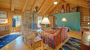 A cozy log cabin interior with a fireplace, wooden furniture, and a green cabinet.