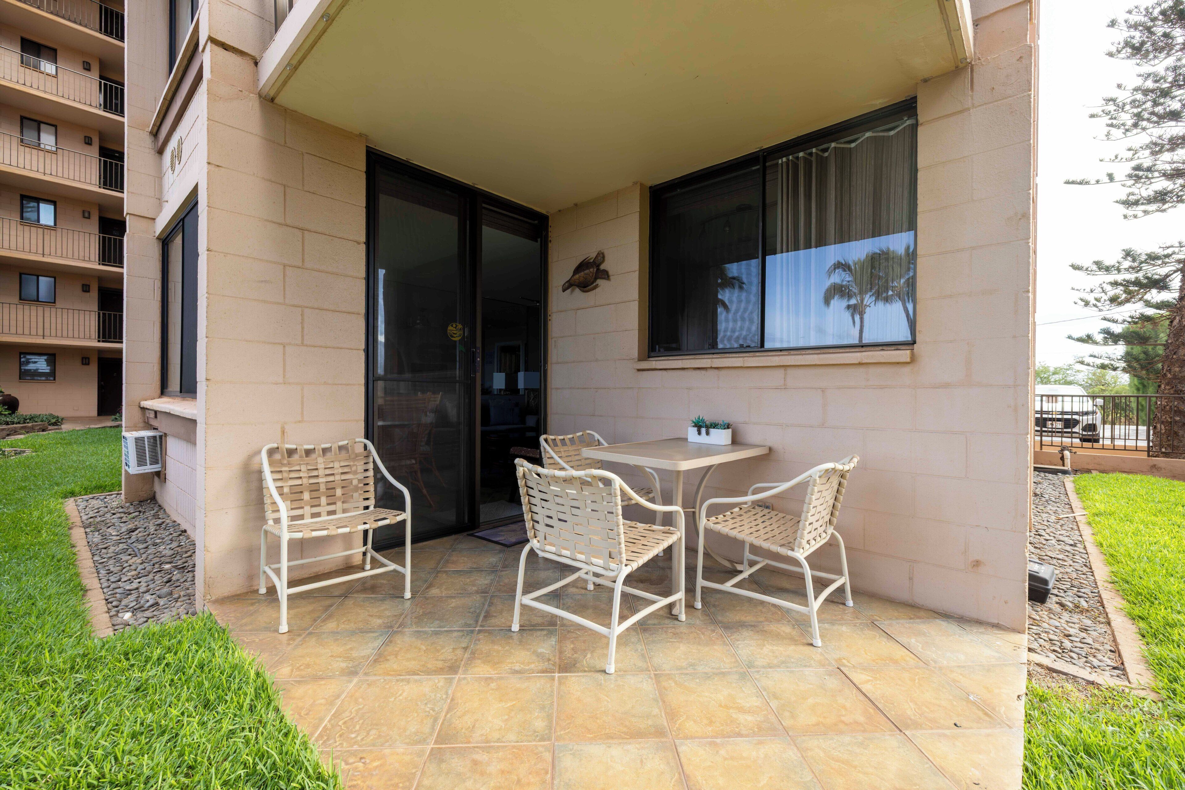 A patio with a table and four chairs, a small potted plant, and a view of palm trees through the window.