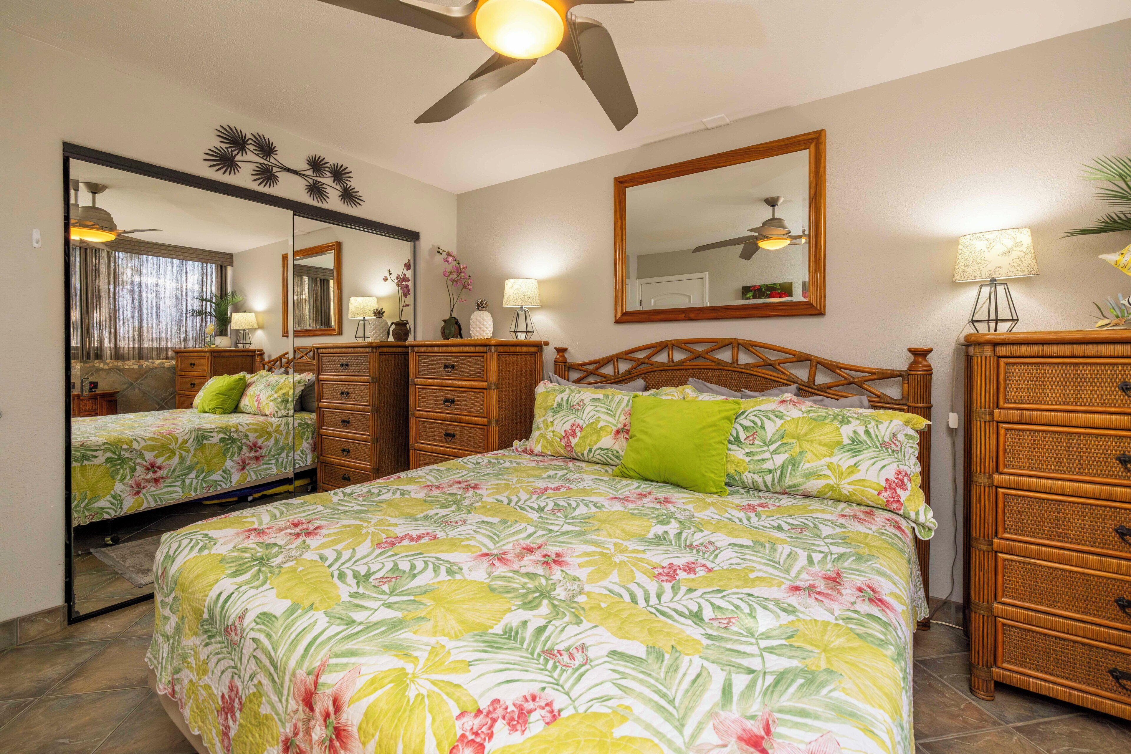 A bedroom with a large bed, two nightstands, a dresser, a ceiling fan, and a mirror.