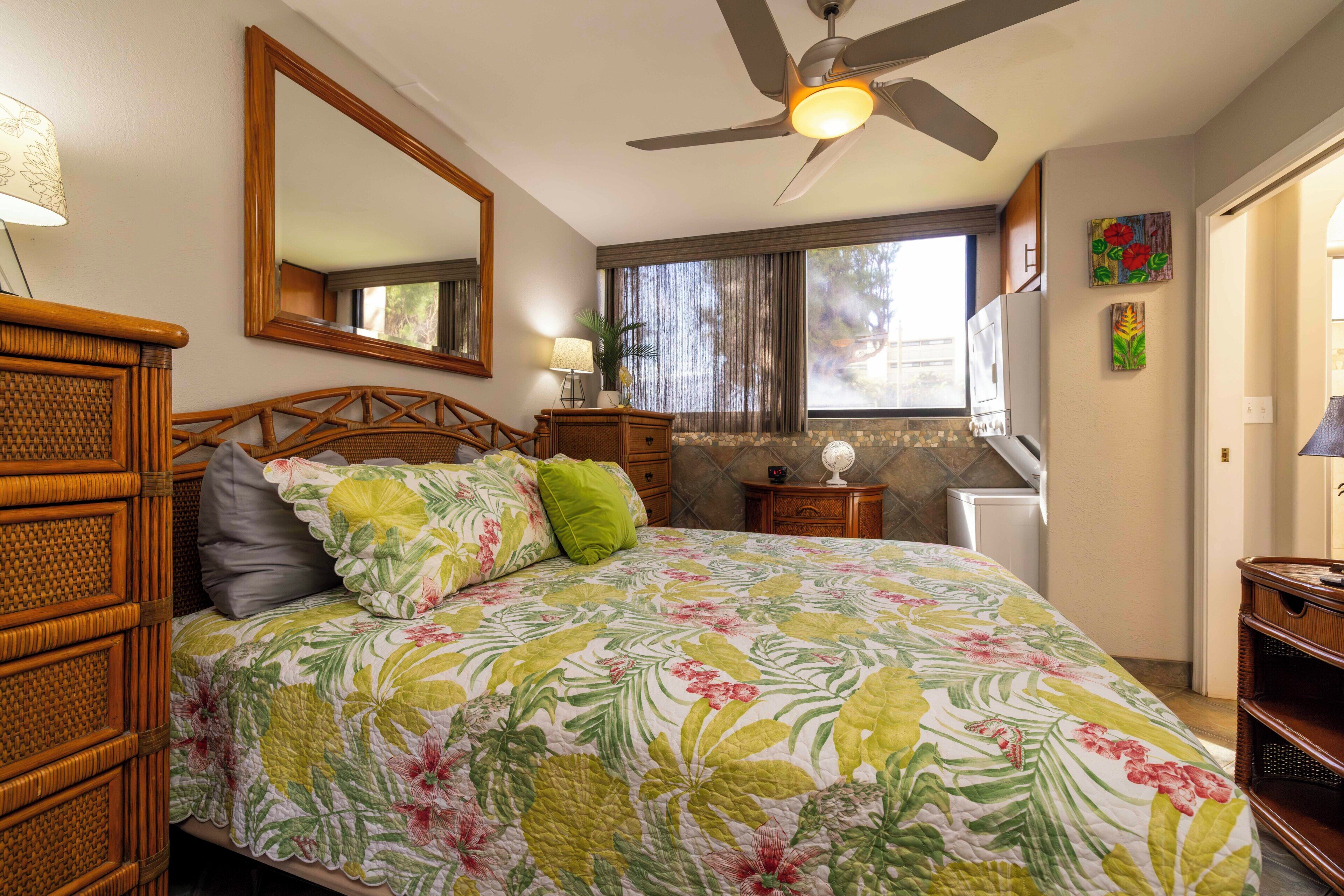 A bedroom with a bed, a ceiling fan, a window with curtains, a dresser, and a mirror.
