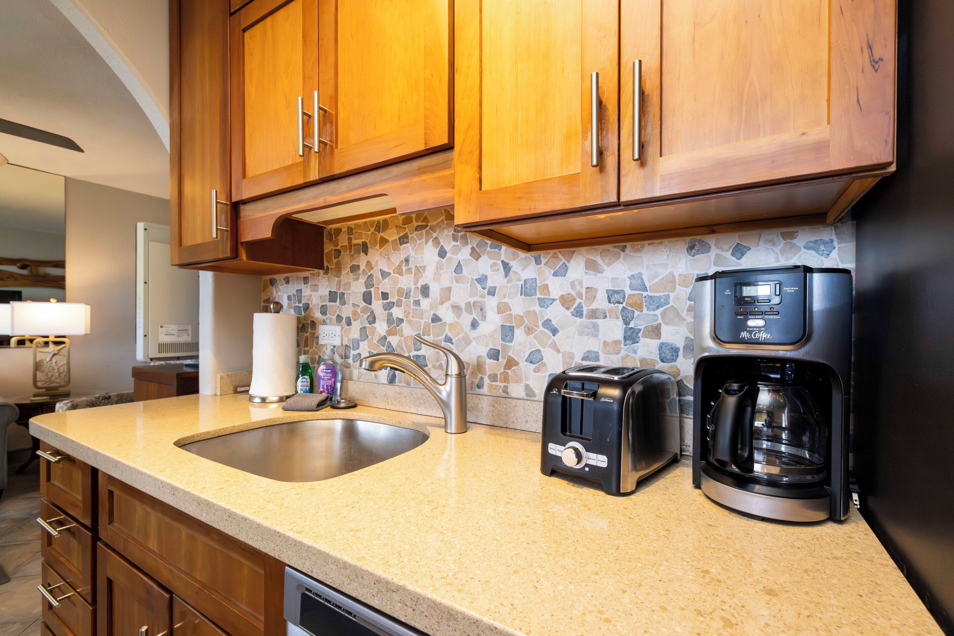 A kitchen with wooden cabinets, a granite countertop, a coffee maker, a toaster, and a stone backsplash.