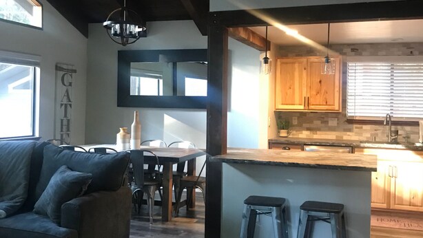 A modern kitchen with wooden cabinets, a bar area with stools, and a dining area with a sofa and chairs.