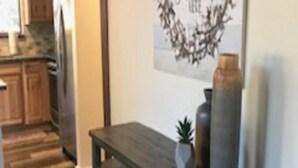A kitchen with wooden cabinets, a dark wooden bench, and a wall decoration with a wreath and text.