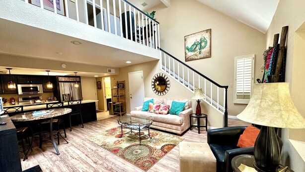 A spacious living area with a high ceiling, a dining area, and a staircase leading to an upper level.