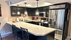 A modern kitchen with dark cabinets, stainless steel appliances, and a central island with bar stools.