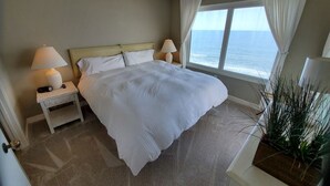 Quarto de hotel com uma cama grande, duas mesas de cabeceira com abajures, uma janela com cortinas e um vaso de planta.