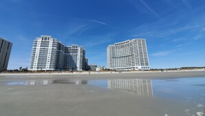 Um hotel à beira-mar com vários edifícios altos, uma praia de areia e céu claro.