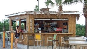 Um bar tiki com teto de palha, balcão e área de estar com cadeiras e mesas.