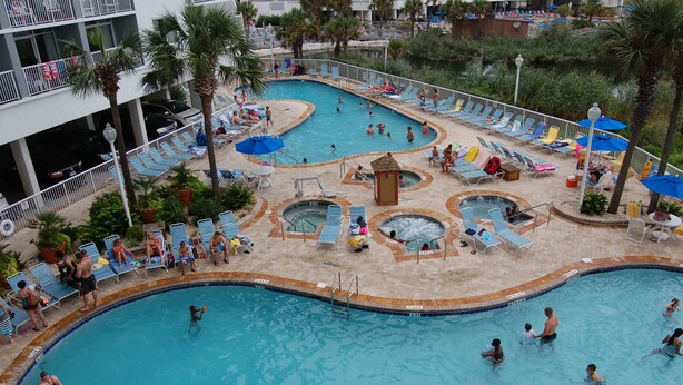 Uma área de piscina com vários níveis, com diferentes atrações aquáticas e espreguiçadeiras.