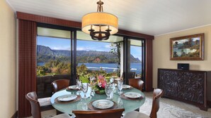 A dining area with a table set for six, large windows offering a view of mountains and a lake, a chandelier, and a decorative cabinet.