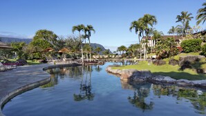 A pool area with lounge chairs, palm trees, and a view of mountains.